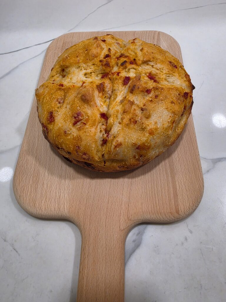 Freshly baked sourdough bread with a crispy golden-brown crust, sun-dried tomatoes, and basil.